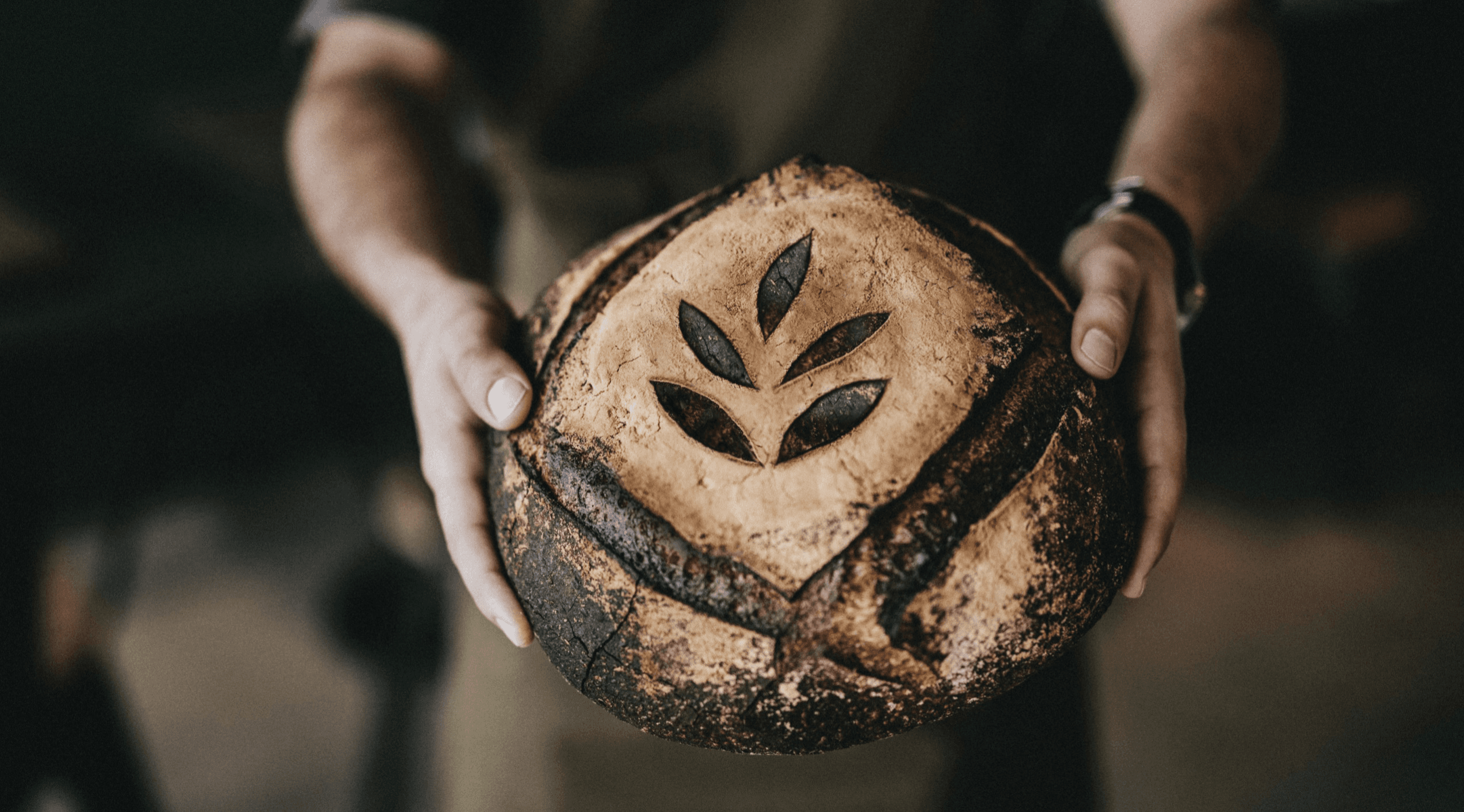 WearebakersV3 Baker holding a boule bread with the Guesa Trading SL logo embedded in it.